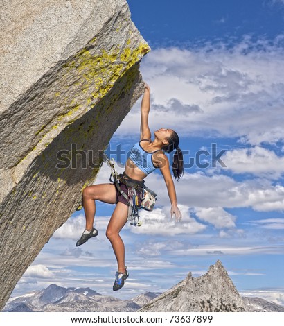 Female rock climber struggles to reach her next grip as she battles her way up a steep cliff.