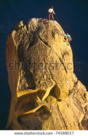 Team of rock climbers struggle to the summit of a steep pinnacle.