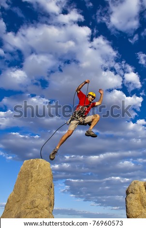 Rock climber leaping from the summit of a steep spire after a successful ascent.