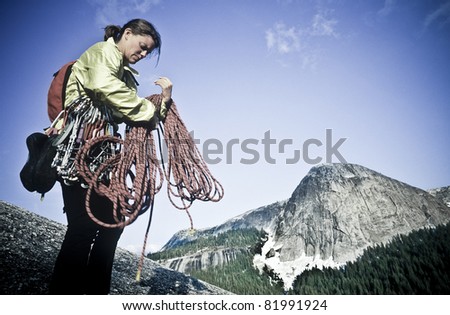 Female climber coils ropes on the summit of a challenging cliff.