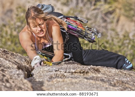 Female rock climber struggles for her next grip on a challenging ascent.