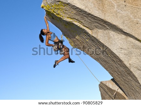 Female rock climber struggles to grip the edge of a challenging overhang.
