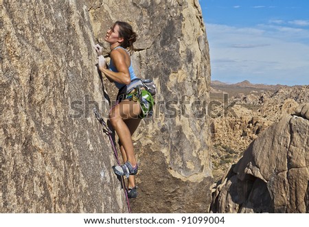 Female rock climber struggles to grip the edges on a challenging cliff.