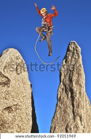Rock climber leaping from the summit of a steep spire after a successful ascent.