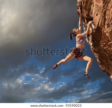 Female rock climber struggles to reach her next grip  on the edge of a challenging cliff.