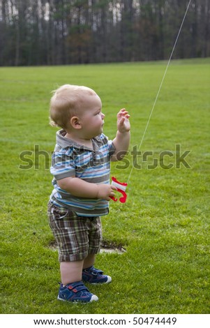 A very young toddler boy learning to fly a kite.