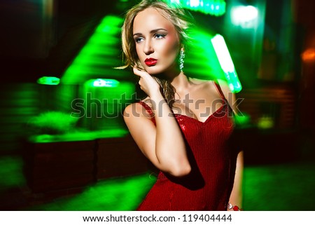 Beautiful woman posing in front of shop windows of illuminated city at night, pulsed light, continuous exposure