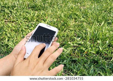 blur hand using mobile phone on fresh grass in day light background
