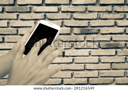 blur hand touching mobile phone on old dirty brick wall background in vintage tone