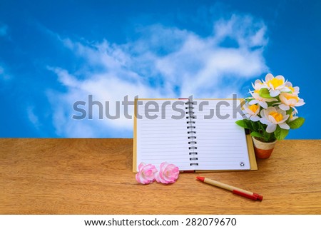 open notepad and flower vase on blur cloud on blue sky background
