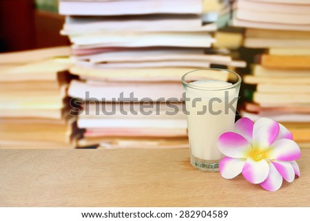 glass of milk and purple flower on blur stacking book background