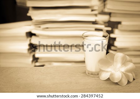 glass of milk and purple flower on blur stacking book background