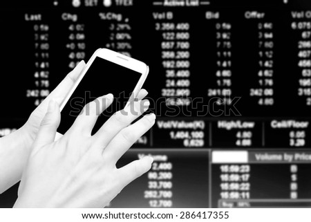 blur hand touching mobile phone over blur stock market number background  in black and white tone