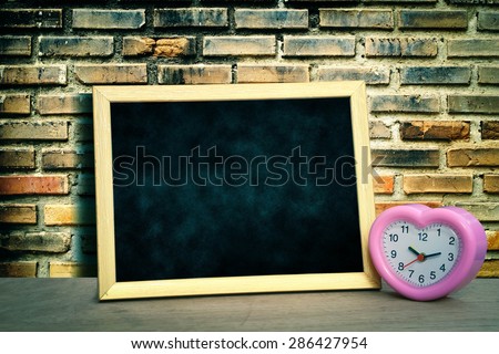 grunge blackboard and pink clock on old dirty brick wall background in vintage tone