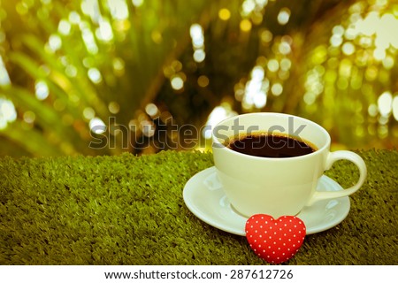 close up image of coffee and red heart on turf with blur palm leaf background