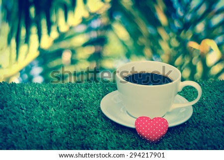 coffee and small red heart on turf with blur image of palm tree background
