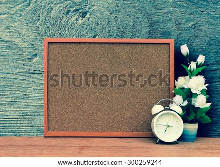 blur cork board with white clock and flower vase with grey wooden plate background ,green vintage tone