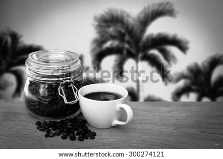 glass pot of coffee seed and cup of coffee with blur palm tree ,black and white tone