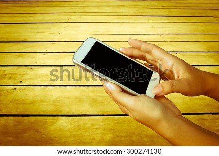 hand of child using mobile phone with wooden floor background  ,vintage tone