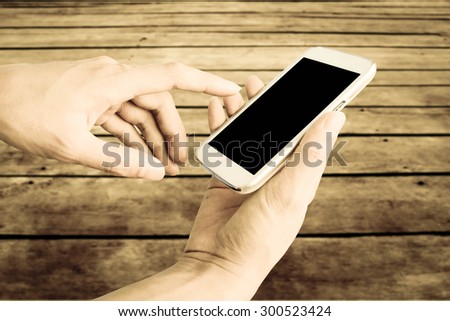 hand of man using mobile phone with blur wooden floor background ,vintage tone