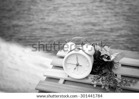 white clock and flower on the table with blur dark beach background ,black and white tone