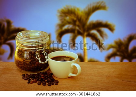 glass pot of coffee seed and cup of coffee with blur palm tree