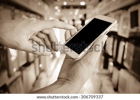 hand of man using mobile phone on blur shop background ,vintage tone