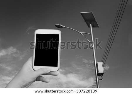 blur hand holding mobile phone  on solar cell street lamp background  ,black and white tone