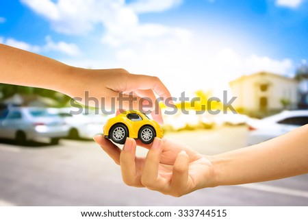 hand holding car model on blur outdoor car park with yellow light