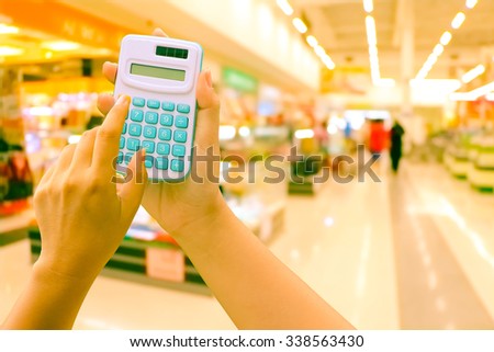 hand hold and point at blue calculator on blur store background vintage  tone