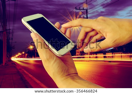 hand of man using mobile phone with traffic light and road