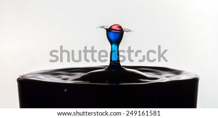 Red water drop splashing and colliding into a rebounding blue water droplet coming out of black water.