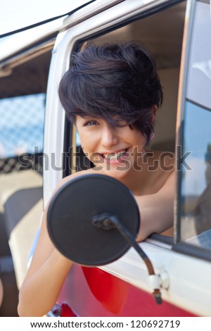 a sun tanned young girl with short hair cut and blue eyes sitting in front of the side view mirror is smiling for the camera