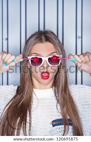 portrait of a young long-haired beautiful girl is holding two red lollipops in front of the white sunglasses
