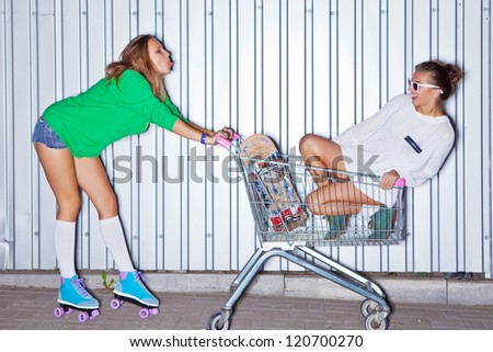 a beautiful young girl in sexy shorts, stockings and roller skates is showing out her tongue to a beautiful girl in a supermarket trolley