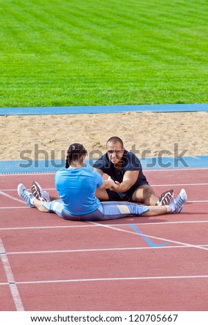 Two athletes helps each other to stretch in the stadium on a sunny day