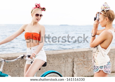 one beautiful tanned girl takes picture of her blonde sexy friend on city bike at sea shore