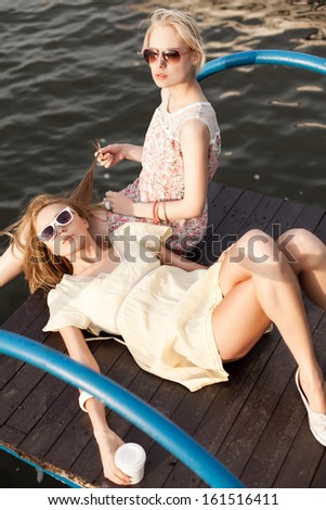 one beautiful girl lies on her girlfriend's knee holding to-go cup while her friend plays with her hair