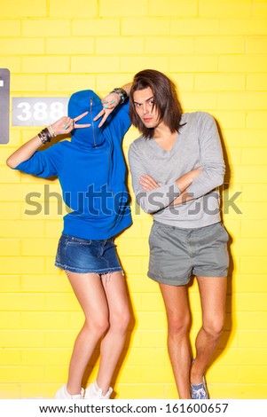 a girl in blue hoodie and boy have fun and grimace in front of yellow brick wall
