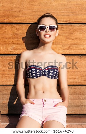 beautiful good shaped girl in white sunglasses poses against wooden wall