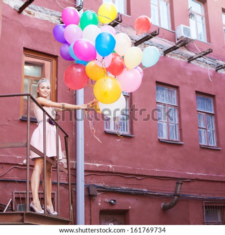 beautiful girl in pink dress holds a bunch of balloons in front of old building