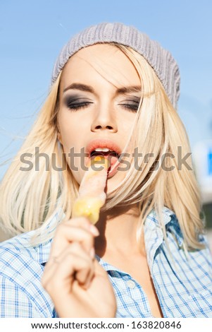 Portrait of beautiful blond girl with closed eyes and smokey eye makeup who enjoys licking ice cream with her tongue