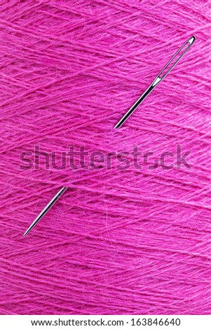 close up of long stainless needle stuck in purple wool texture thread