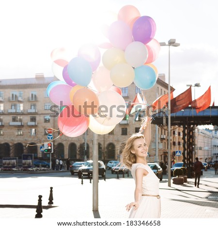 beautiful blonde girl with long legs in summer dress holds a bunch of multicolored balloons