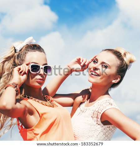 two young girls in summer outfit pose for the camera against the blue sky