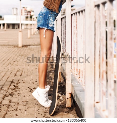 young beautiful girl with long legs and silky hair in denim short overalls stands on tiptoes hanging over bridge