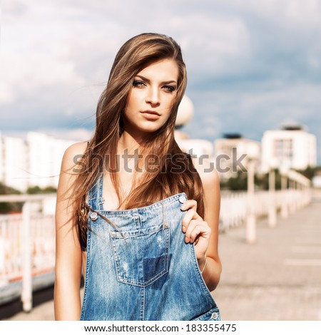 beautiful girl with long silky hair in denim short overalls holding front part of it