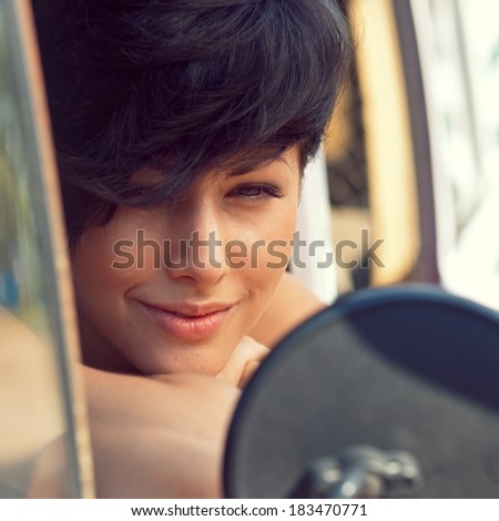 a beautiful young girl with short hair cut and blue eyes is looking into the side view mirror