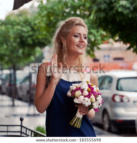 a beautiful young blond girl in summer dress with a bunch of flowers is waving to her friends