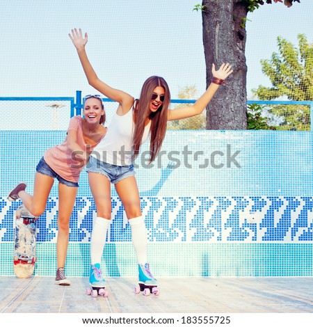 two beautiful young girls on the floor of an empty pool, one pushes the other in roller skates